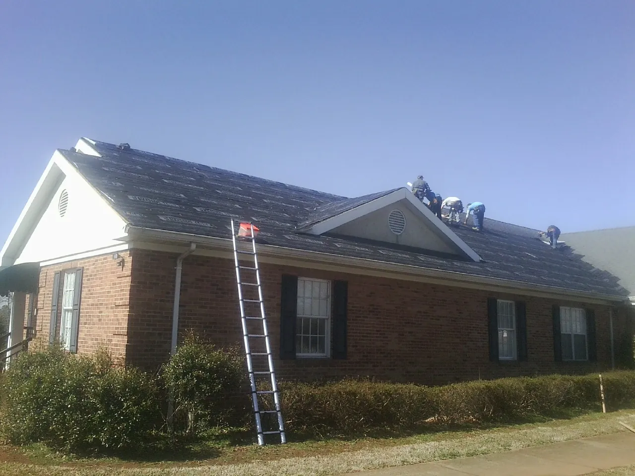 Crew tearing shingles off a brick ranch roof with a ladder set — Metal Roof Repair work by our crew in Midlothian